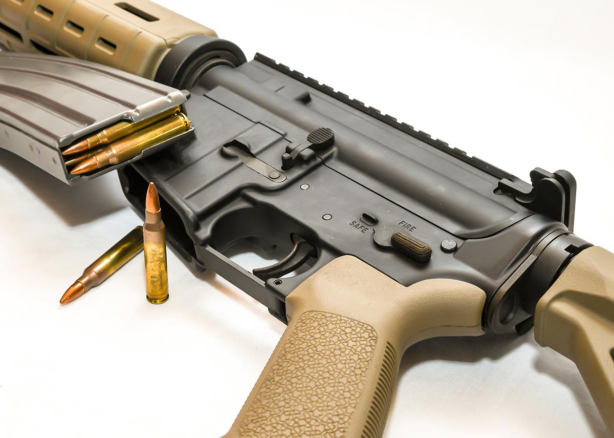 Magazine Being Loaded into Firearm with Two Bullets in Front of It on White Background